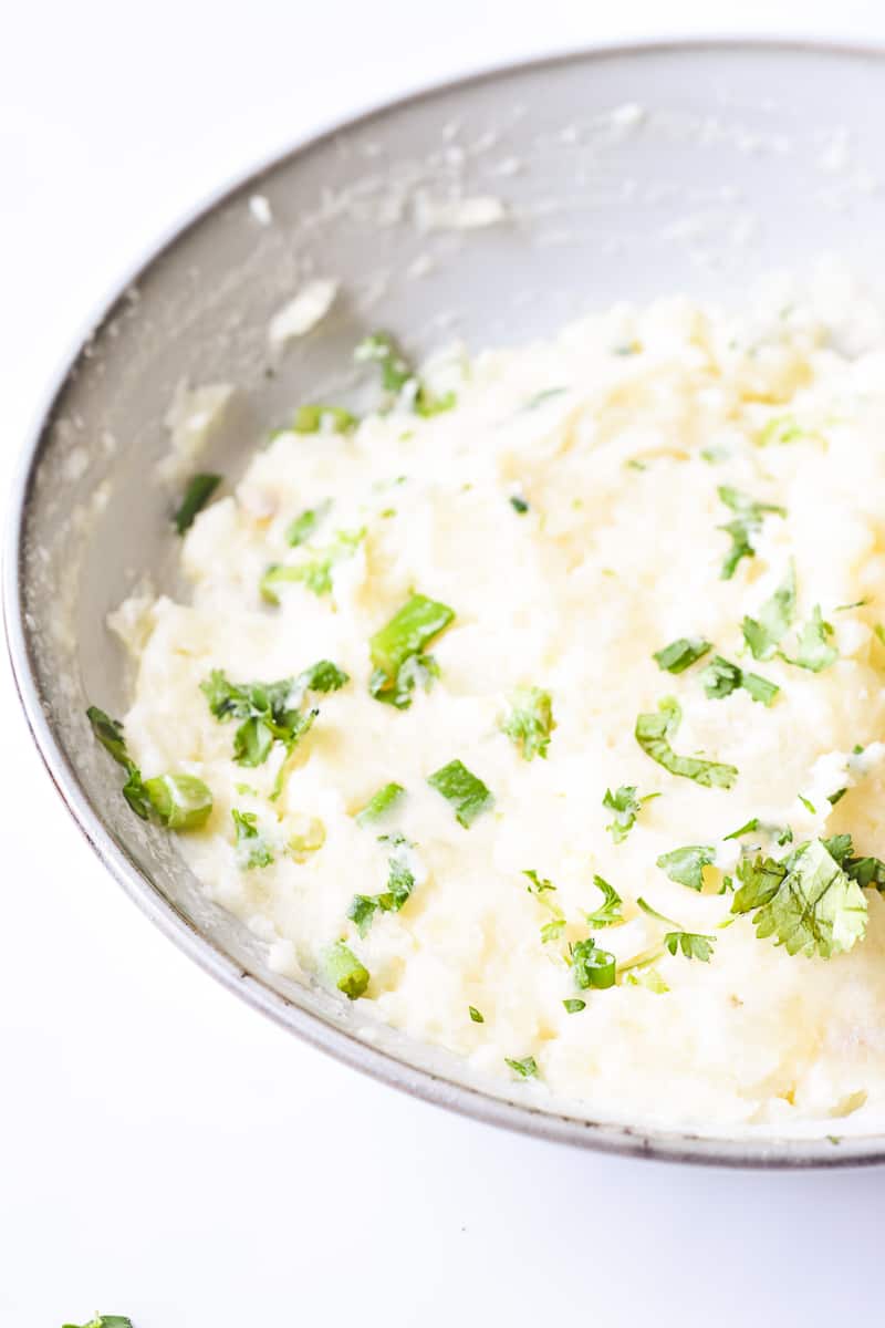 creamy, fluffy mashed potatoes garnished with cilantro and spring onion.