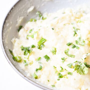 creamy, fluffy mashed potatoes garnished with cilantro and spring onion.